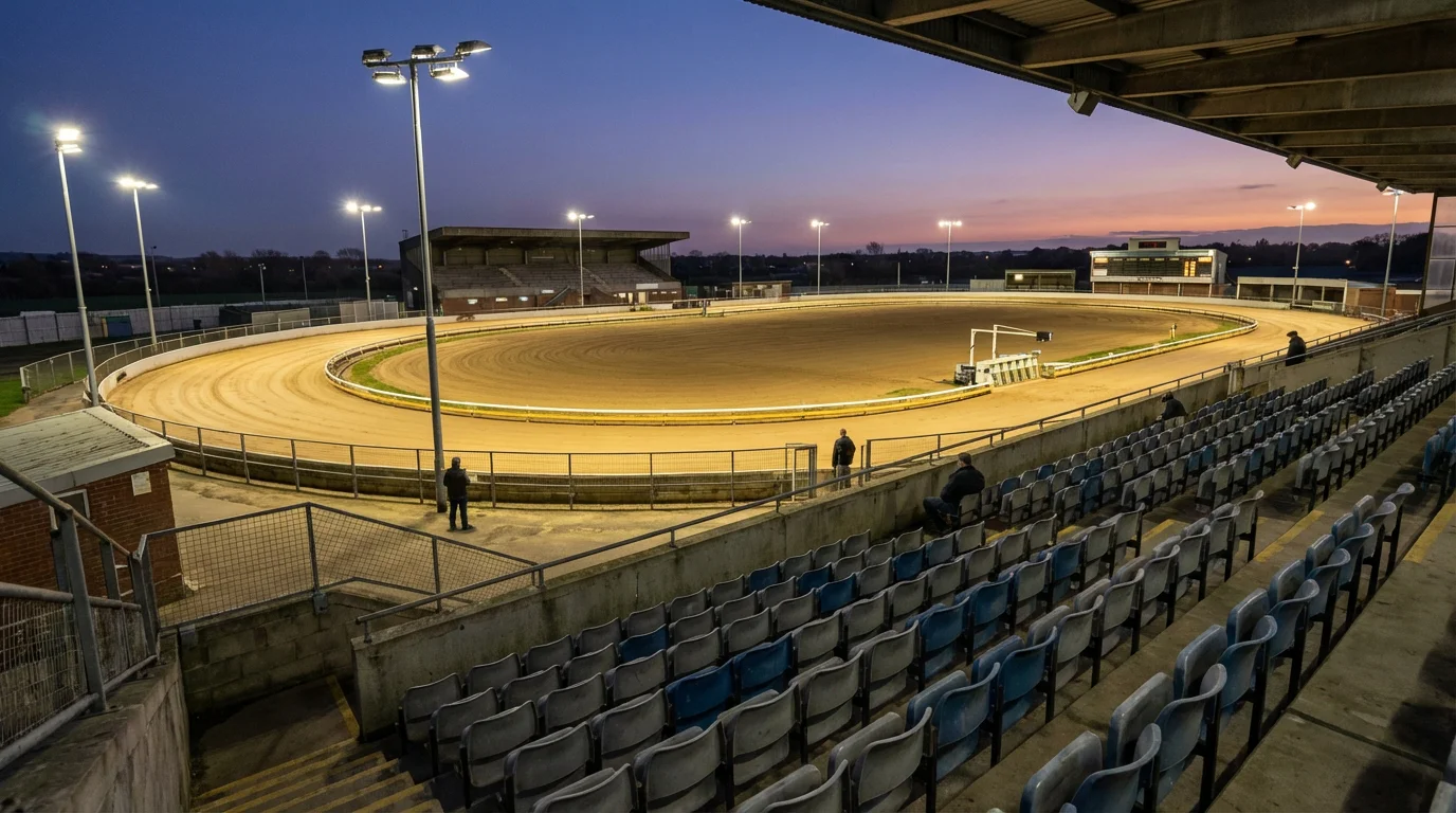 Wide view of an empty UK greyhound racing stadium showing the oval sand track, grandstand seating, and floodlight towers